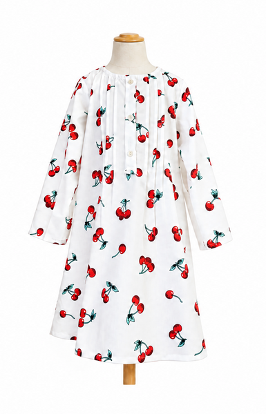 A white long-sleeve dress with a red cherry print, displayed on a wooden dress form against a plain white background.