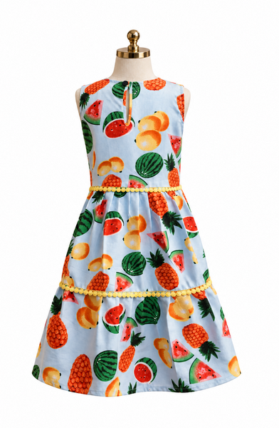 A sleeveless light blue dress displayed on a mannequin, featuring a colorful fruit print with watermelons, pineapples, and peaches, accented with yellow beaded trim at the waist and hips.