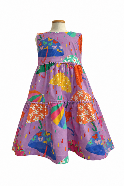 A sleeveless tiered dress displayed on a mannequin torso against a plain white background. The dress has a lavender-purple base with a colorful print of umbrellas, flowers, raindrops, and small decorative motifs in blue, green, yellow, orange, pink, and white.