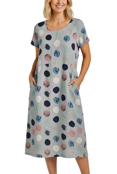 A woman wearing a short-sleeve, knee-length shift dress with a gray base and a multicolor abstract polka dot pattern, standing against a plain white background.