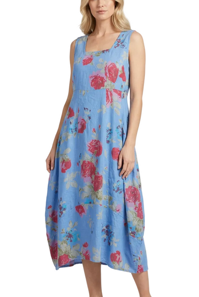 A woman modeling a sleeveless midi dress with a light blue base and a pink and red floral print, paired with beige heeled sandals, against a light gray studio background.