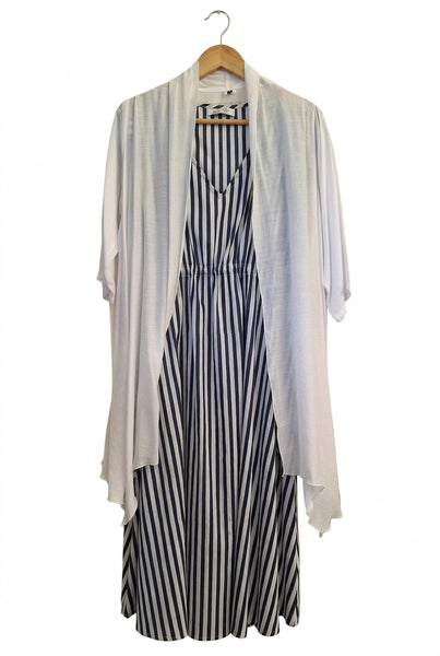 A women's sleeveless dress with a black and white striped pattern, layered over a white long-sleeve shirt, laid flat on a cream-colored fabric background.